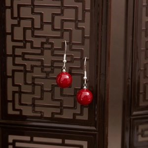 Detail of red beaded drop earrings with silver hooks against a vintage wooden screen