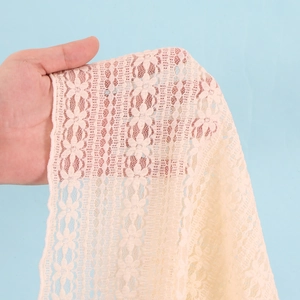 Close-up of light pink lace fabric showing intricate floral patterns and transparency
