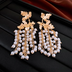 Elegant gold maple leaf earrings with white pearl tassels on a luxury silk background