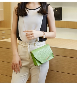 Detail shot of bright green crocodile pattern chain bag worn on a shoulder