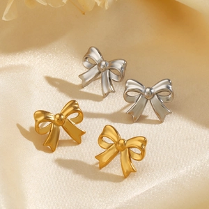 18K gold and silver stainless steel bow earrings on elegant beige silk background