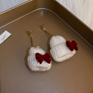 Detail view of mini white knitted hat earrings with red velvet bow and golden star stud