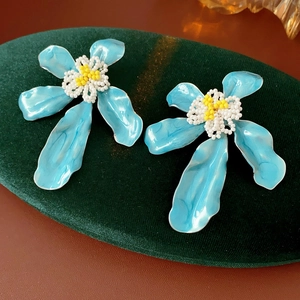 Détail de boucles d'oreilles fleurs en émail bleu avec perles blanches et jaunes