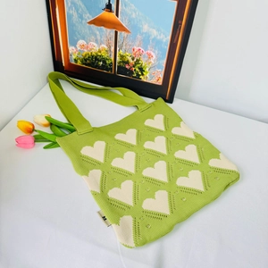 Green knitted tote bag with white heart patterns shown with tulip flowers and frame