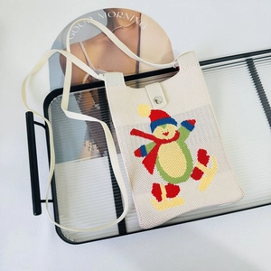 Detailed close-up of a cream-colored knitted snowman crossbody bag on a glass tray