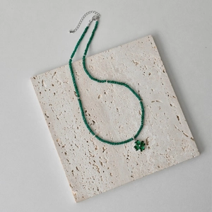 Macro detail of a green beaded S925 silver necklace with a clover pendant on stone
