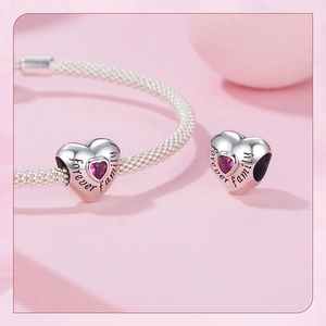 Macro detail of silver heart charm with pink zircon and forever family engraving