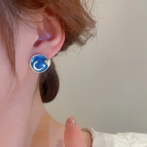 Detail of blue enamel earring featuring a crescent moon and golden heart with wavy borders