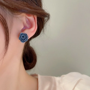 Close-up of a model wearing navy blue rose-shaped stud earrings in a vintage style