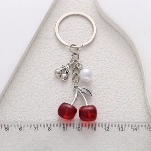 Sweet red cherry keychain with pearls and silver leaves on a textured beige background