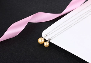 Macro shot of two golden pearl pendants on a fine silver chain over a white ceramic tray
