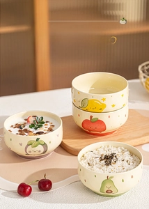 Close-up of four ceramic bowls featuring cute cartoon fruit patterns in a warm setting