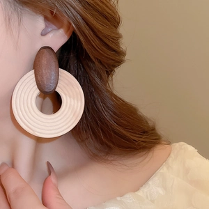 Detail of large brown wood and ivory textured hoop earring worn by a model in a side view