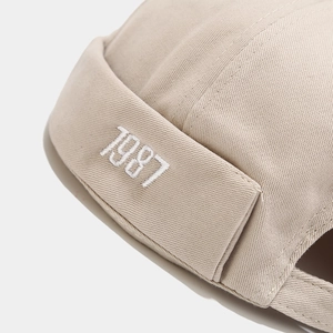 Vista dettagliata del ricamo bianco 1987 su un cappello docker beige in twill di cotone