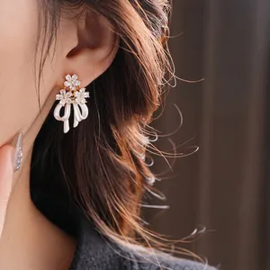 Boucles d'oreilles fleurs et nœuds en plaqué or avec zircons portées par mannequin