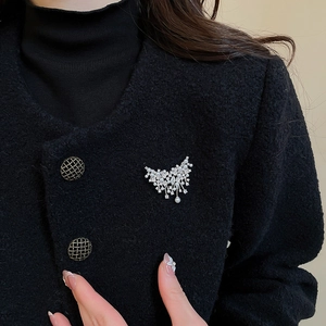 Close-up of a silver zircon butterfly pearl brooch on a black tweed coat fabric