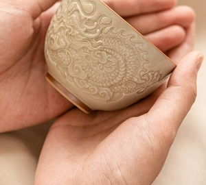 Detailed macro of beige ceramic tea cup featuring intricate embossed dragon relief pattern