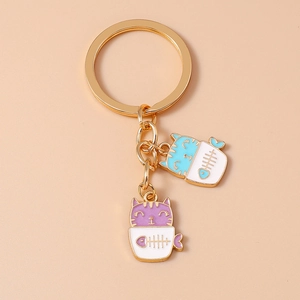 Golden keychain with cute blue and purple enamel cats in white cups on beige background