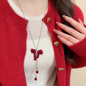 Close-up of red flocked bow necklace with zircon detail on red knit cardigan