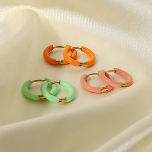 Tres pares de pendientes de aro de esmalte de colores naranja, verde y rosa sobre seda blanca