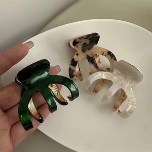 Close-up of three acetate hair claws in dark green, tortoiseshell, and pearl white colors