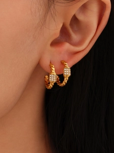 Close-up of golden twist hoop earrings with sparkling rectangular zircon on model ear