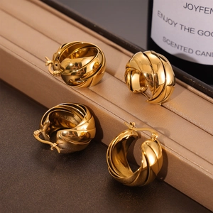 French luxury gold-plated twisted hoop earrings displayed on a beige leather stand