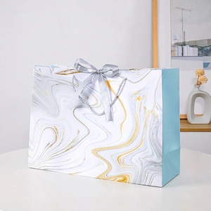 Elegant marble pattern gift bag with grey silk ribbon handle on minimalist white stand
