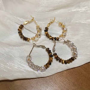 Close-up of gold and silver tiger eye earrings with sparkling zircon on silk fabric
