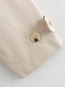 Détail du tissu sergé et des boutons ambrés sur un trench-coat de couleur beige clair