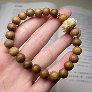 Détail d'un bracelet en bois de santal avec perle de lotus sculptée devant un livre