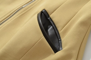 Macro detail of khaki twill jacket featuring black leather trim on pocket and metal zipper