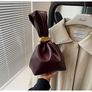Detail of burgundy leather bucket bag with gold metal clasp and drawstring closure