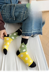Detail of yellow and green cotton mid-tube socks with white polka dots on a wooden floor
