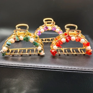 Golden metal hair claw clips with amethyst, green stones, and pearls on a dark background
