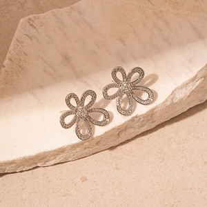 Macro detail of silver floral stud earring with sparkling zircon on natural stone