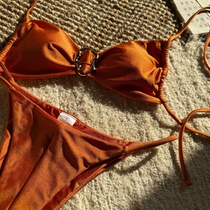 Detail eines orangefarbenen Satin-Bikinis mit Metallring und glänzendem Polyestergewebe