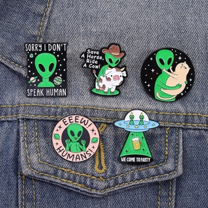 Cartoon green alien enamel pins set on blue denim jacket featuring five creative space designs