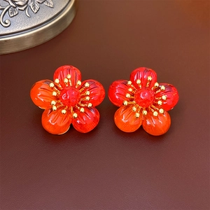 Macro shot of red five-petal flower earrings with gold center on brown leather surface