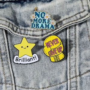 Detailed close-up of three enamel motivational lapel pins on a denim jacket pocket