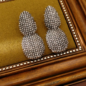 Dettaglio degli orecchini vintage a goccia con pavé su elegante tessuto verde oliva