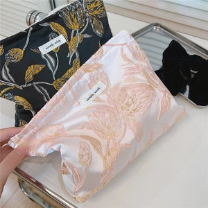 Nahaufnahme der Blumenstickerei auf schwarzen und rosa Satin-Kosmetiktaschen für Reisen