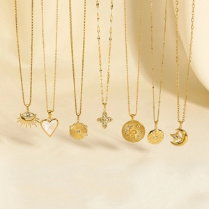 Detail of seven gold-plated necklaces with charms like sun eye and heart on silk fabric