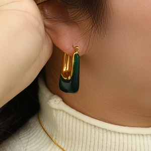 Close-up of gold and dark green U-shaped acrylic earrings worn on a model's ear
