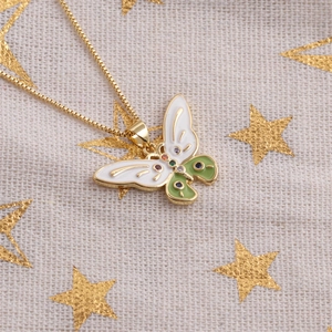 Detail of a gold butterfly pendant with white and green enamel and sparkling zircon accents