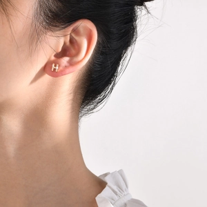 Close-up of gold-plated H-shaped stud earring with cubic zirconia on female model