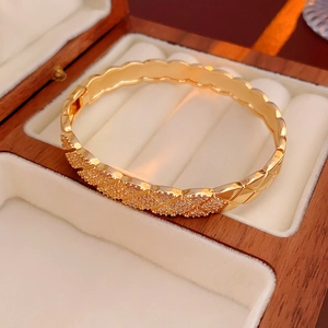 Macro detail of gold quilted lattice bangle with inlaid cubic zirconia in jewelry box