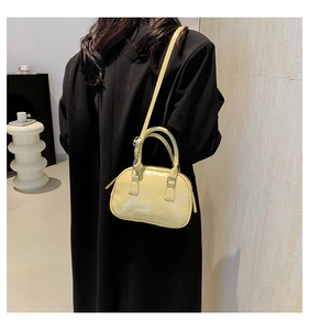 Detail of light yellow bowling bag worn as a crossbody with shiny leather finish
