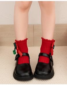 Detail of red Christmas socks with ruffle cuffs, bows, and pom-poms worn with black shoes