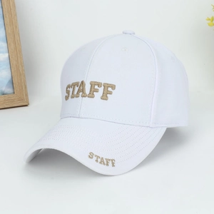 Detail of gold STAFF embroidery on the front of a minimalist white cotton baseball cap